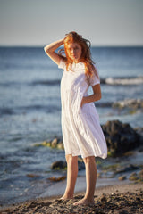 Woman wearing white short sleeve smock linen dress standing on beach with ocean background
