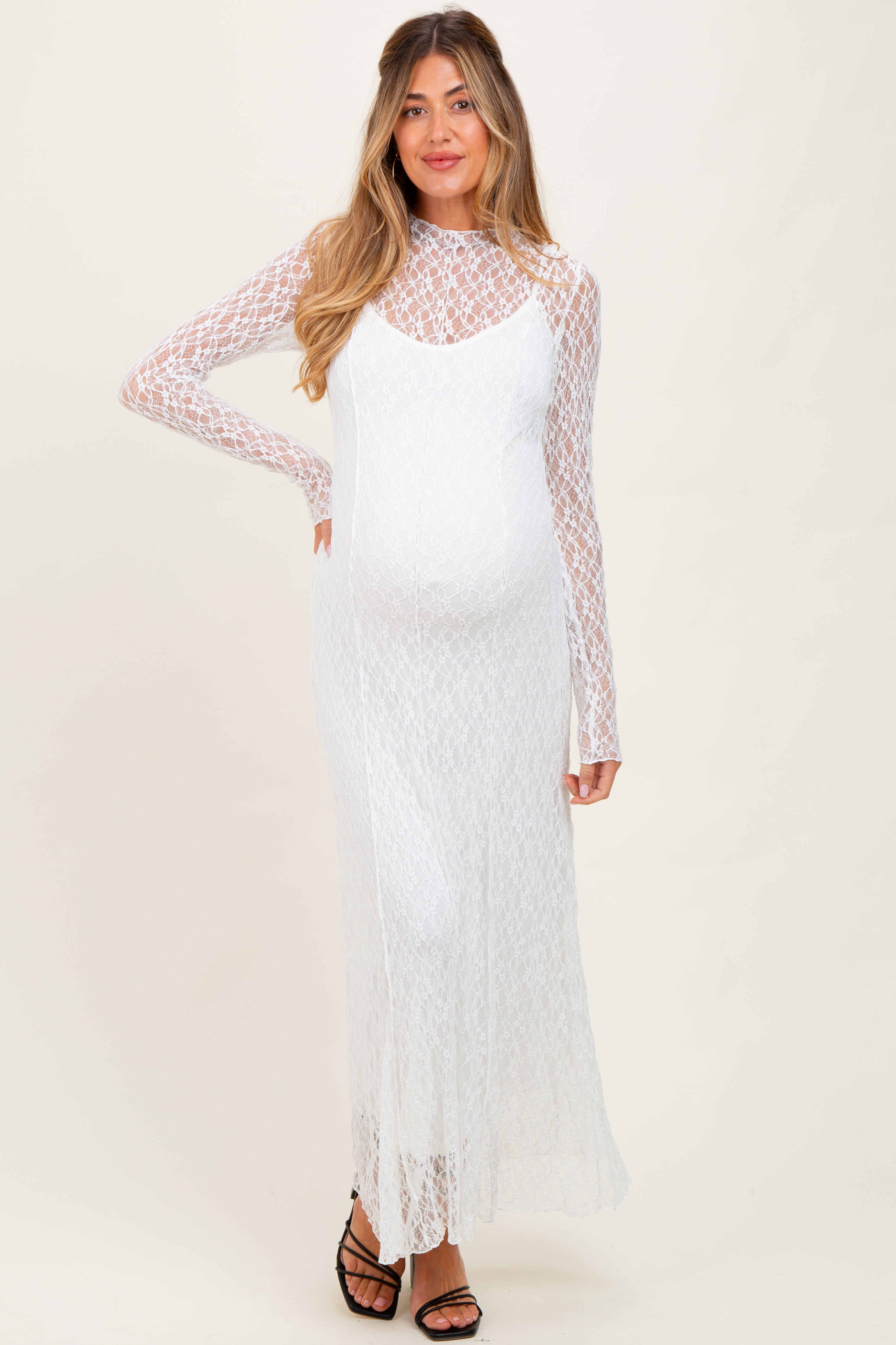 woman wearing a white lace maternity dress with long sleeves and a visible baby bump