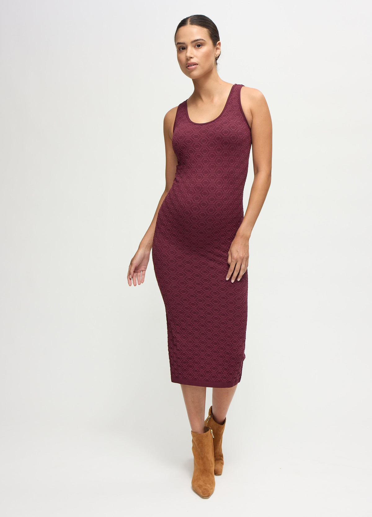 A pregnant woman wearing a fig-color textured bodycon maternity midi dress with tan suede boots